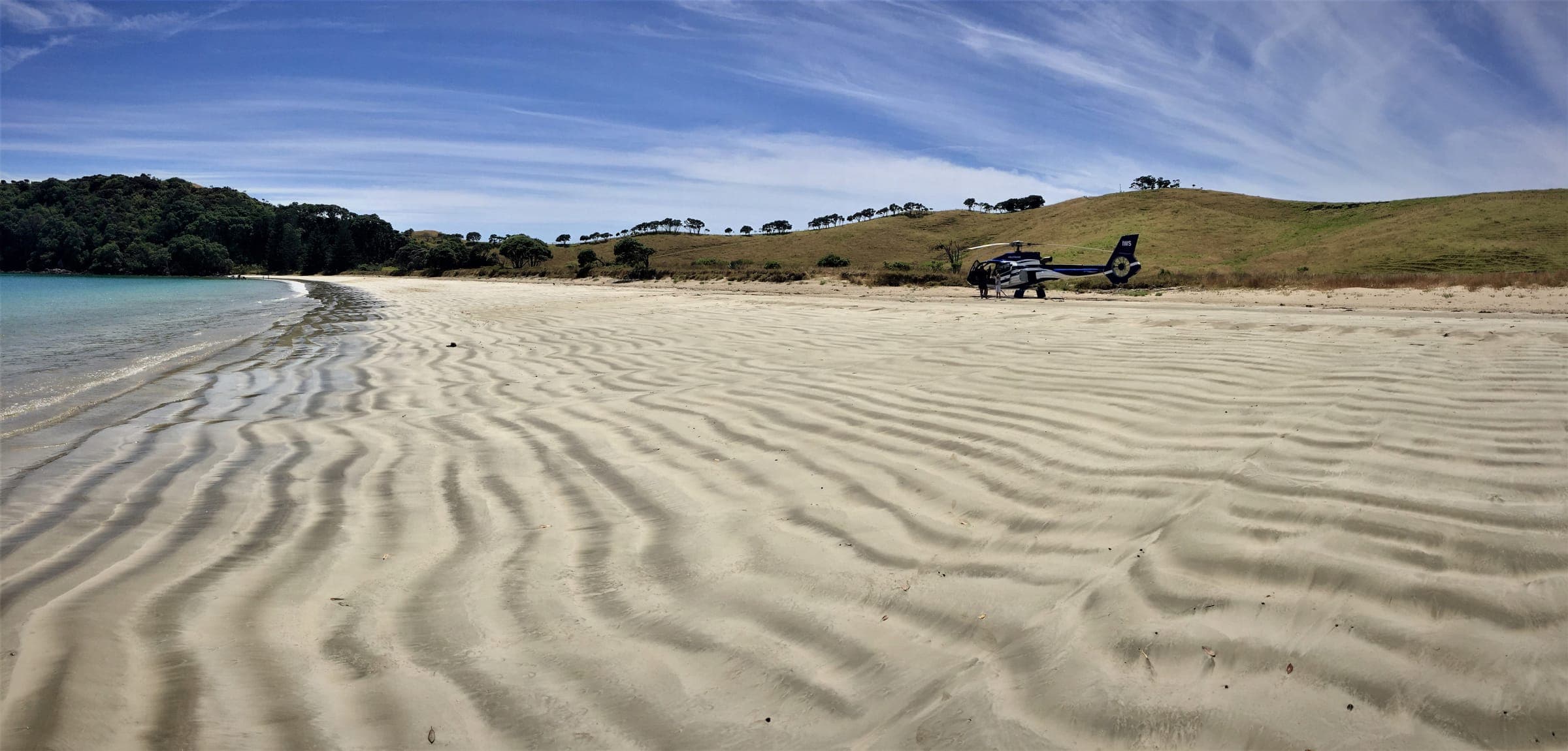 A helicopter parked on a North Island beach, the sand rippled by the tide