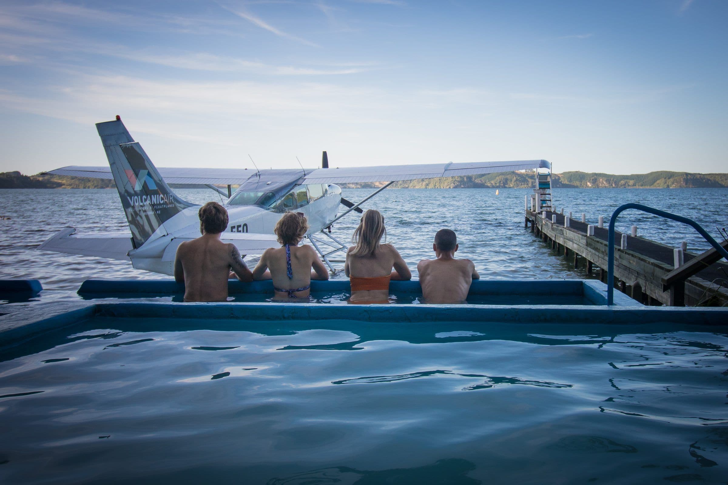 Bathers in a lakeside hot pool on Lake Rotoiti, a floatplane moored alongside